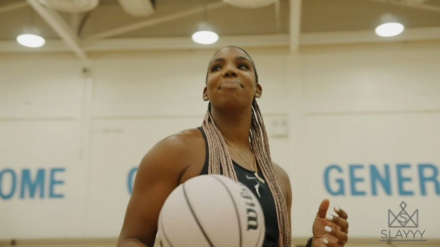 Reshanda Gray holding a basketball in a school gym, wearing pink box braids
