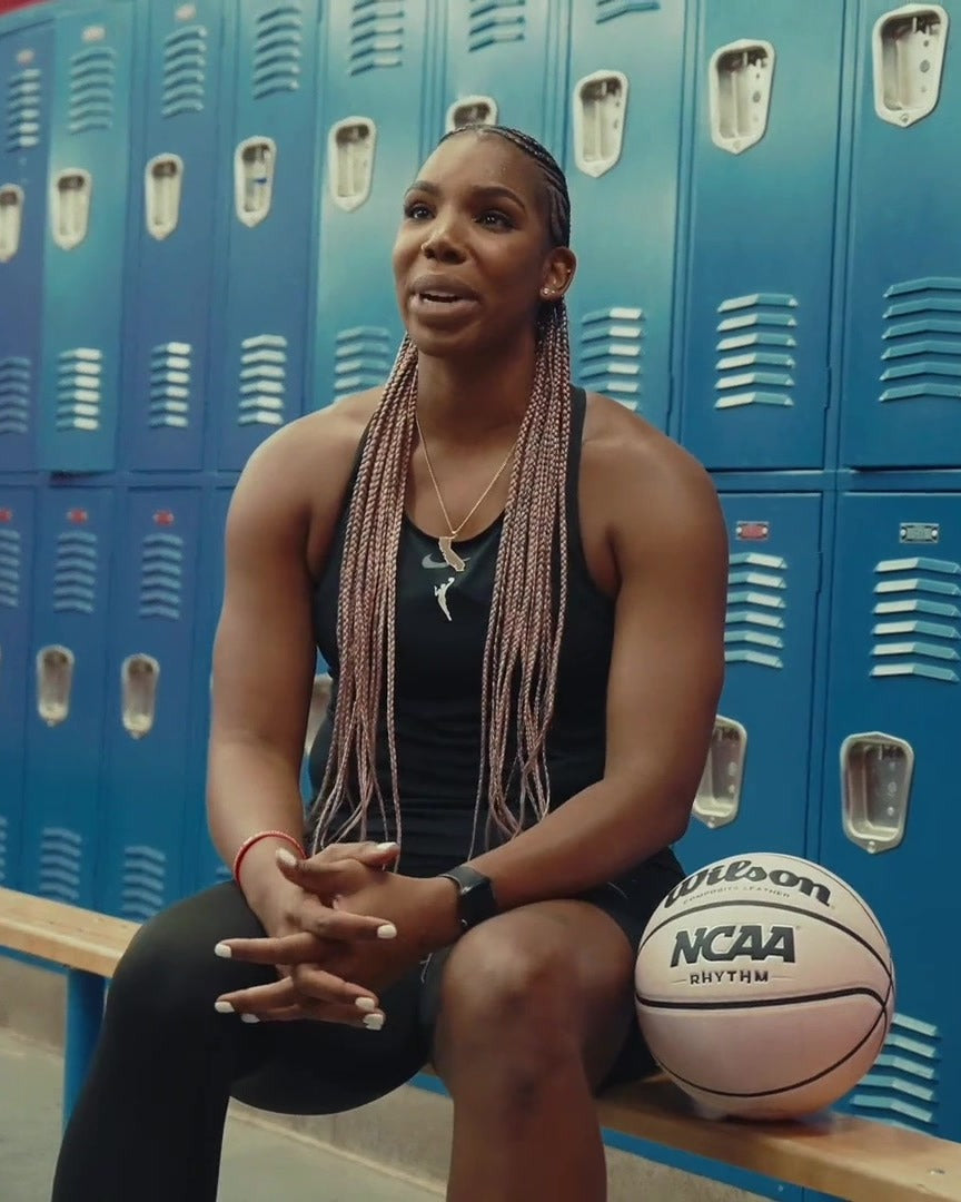 Reshanda Gray seated in a locker room with long pink box braids and a basketball